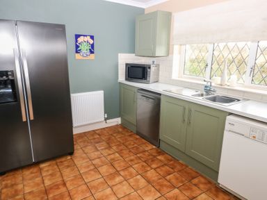 A kitchen with green lower cabinets a stainless steel refrigerator dishwasher microwave and a window with a blind at Greenhaven in Narberth