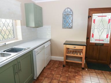A kitchen with green cabinets a white countertop a double sink a dishwasher a wooden storage cart and a wooden door with stained glass at Greenhaven in Narberth