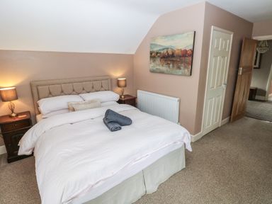 A bedroom with a bed nightstands with lamps a painting on the wall and carpeted floor at Greenhaven in Narberth