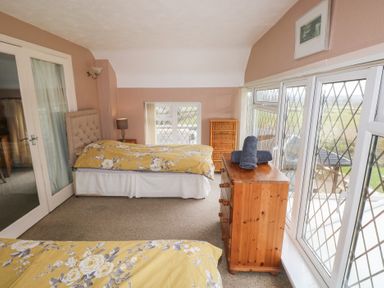 A bedroom with two beds yellow floral bedspreads a wooden chest of drawers and windows with diamond-patterned glass at Greenhaven in Narberth