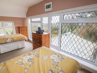 A bedroom with two beds yellow floral bedding a wooden chest of drawers and windows with diamond lattice at Greenhaven in Narberth