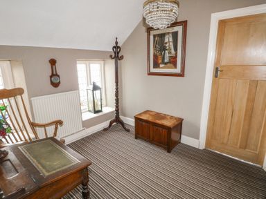 A room with striped carpet wooden chest wooden desk rocking chair coat rack and framed picture at Greenhaven in Narberth