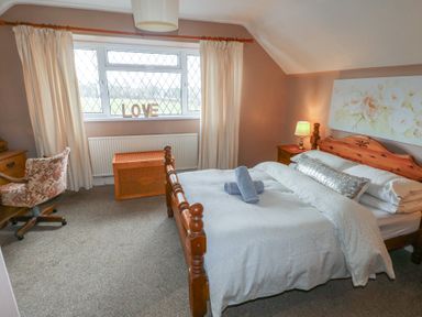 A bedroom with a wooden bed beside a nightstand with a lamp and a window with curtains and a chair at Greenhaven in Narberth
