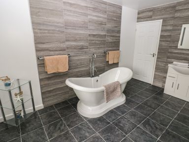 A bathroom with a freestanding bathtub two towel racks a glass shelf and a white vanity unit at Greenhaven in Narberth