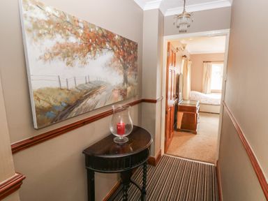 A hallway with a painting above a small dark wood table holding a glass candle holder next to a doorway leading to a bedroom at Greenhaven in Narberth
