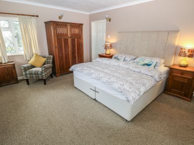 A bedroom with a double bed with pillows and lamps on nightstands and a wooden wardrobe and armchair at Greenhaven in Narberth
