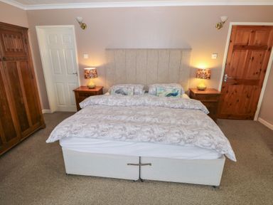 A bedroom with a double bed two bedside tables each with a lamp a wooden wardrobe and two doors at Greenhaven in Narberth