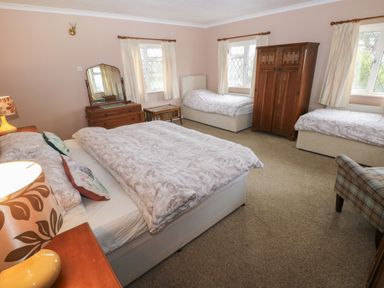 A bedroom with three beds wooden wardrobe dresser with mirror bedside table and a chair at Greenhaven in Narberth