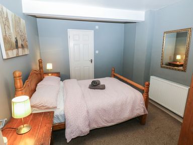 A bedroom with a wooden double bed bedside tables with lamps a mirror on the wall and a painting at Greenhaven in Narberth