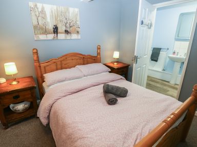 A bedroom with a wooden bed frame pink bedding two bedside tables with lamps and an open door leading to a bathroom at Greenhaven in Narberth