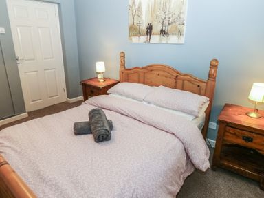 A bedroom with a wooden double bed with pink bedding two bedside tables with lamps and a painting on the wall at Greenhaven in Narberth