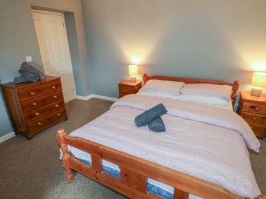 A bedroom with a wooden double bed with two rolled towels on it two bedside tables with lamps and a chest of drawers at Greenhaven in Narberth