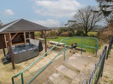 An outdoor patio area with a hot tub under a wooden canopy wooden picnic tables a drum barbecue grill and a grassy garden at Greenhaven in Narberth