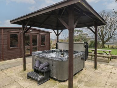 An outdoor covered hot tub with towels and a bottle with glasses next to a wooden shed and picnic bench at Greenhaven in Narberth