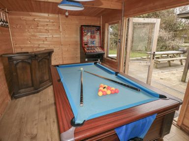 A wooden game room with a pool table two cues and balls a slot machine a wooden cabinet and an open door leading outside at Greenhaven in Narberth