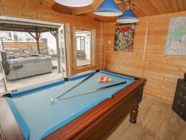 A game room with a pool table and two cue sticks posters on wooden walls and a hot tub outside at Greenhaven in Narberth