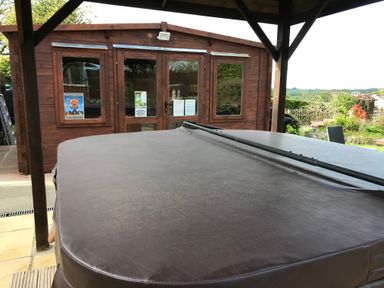 A covered hot tub under a wooden pergola with a wooden cabin and garden in the background at Greenhaven in Narberth