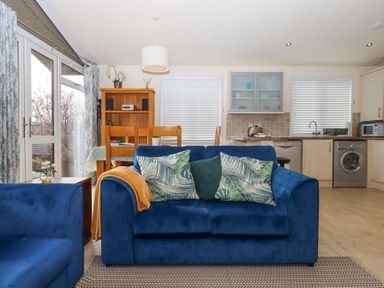 A living room with blue couches and a dining table next to a kitchen at Matilda Lodge in Newton Ferrers