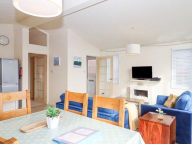 A living room with blue sofas a television and a dining table with wooden chairs at Matilda Lodge in Newton Ferrers