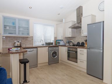 A kitchen with cabinets a washing machine oven refrigerator and microwave at Matilda Lodge in Newton Ferrers