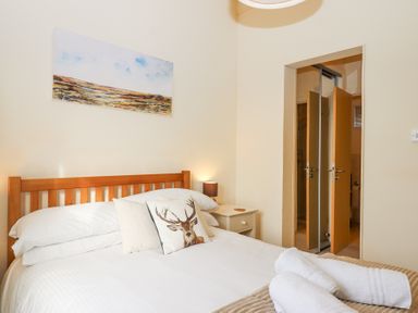 A bedroom with a wooden bed frame white bedding pillows a bedside table and an open door at Matilda Lodge in Newton Ferrers