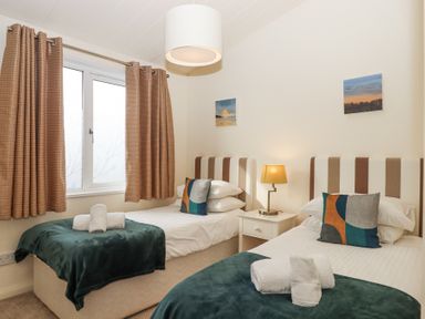 A bedroom with two single beds with pillows and blankets a nightstand with a lamp between the beds and a window with curtains at Matilda Lodge Newton Ferrers