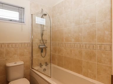 A bathroom with a bathtub shower combination a toilet and a window with blinds at Matilda Lodge in Newton Ferrers