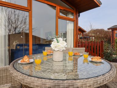 An outdoor glass table with wicker chairs a vase with flowers four croissants on plates and four glasses of orange juice at Matilda Lodge in Newton Ferrers