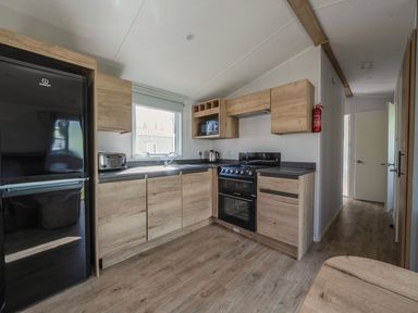 A kitchen with modern appliances and wooden cabinets at Sand and Splash - Hayling Island
