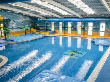 An indoor swimming pool with slides and a mural of trees and birds at Ripples & Reeds - Billing Aquadrome in Billing Aquadrome Holiday Park