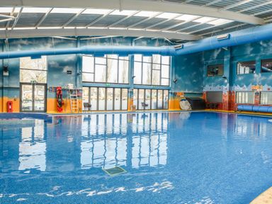 An indoor swimming pool with blue tiled floor and large windows with emergency exit doors at Ripples & Reeds - Billing Aquadrome in Billing Aquadrome Holiday Park