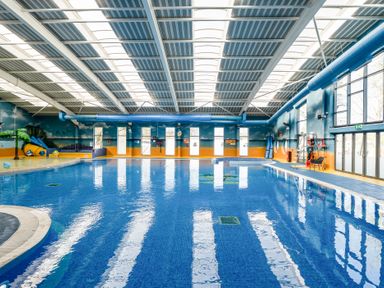 An indoor swimming pool with high windows and water slides at Ripples & Reeds - Billing Aquadrome in Billing Aquadrome Holiday Park