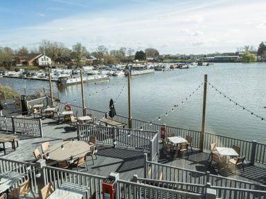 An outdoor seating area with tables and chairs next to water with boats docked at a marina at Ripples & Reeds - Billing Aquadrome in Billing Aquadrome Holiday Park