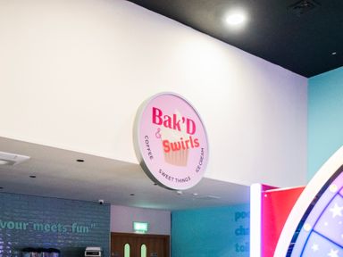 An indoor wall with a round sign reading Bak'D swirls coffee sweet things ice cream at Billing Aquadrome Holiday Park