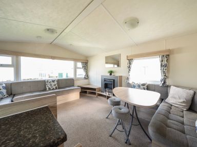 A living area with two sofas a wooden table two stools a fireplace and windows with curtains at Ripples & Reeds - Billing Aquadrome in Billing Aquadrome Holiday Park