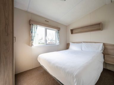 A bedroom with a double bed white bedding wooden headboard a window with curtains and a wooden wardrobe at Ripples & Reeds - Billing Aquadrome