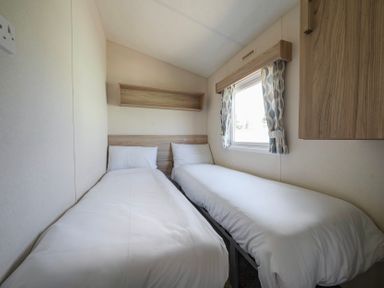 A bedroom with two single beds a window with patterned curtains and wooden shelves at Ripples amp Reeds - Billing Aquadrome in Billing Aquadrome Holiday Park