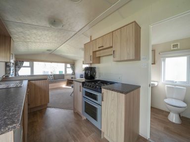 A kitchen with wooden cabinets and appliances next to a bathroom with a toilet and window at Ripples & Reeds - Billing Aquadrome in Billing Aquadrome Holiday Park