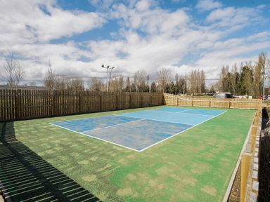 An outdoor sports court with green and blue surface surrounded by a wooden fence and trees at Ripples & Reeds - Billing Aquadrome in Billing Aquadrome Holiday Park