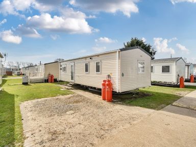 A group of mobile homes on a grassy and gravel area under a blue sky at Ripples & Reeds - Billing Aquadrome in Billing Aquadrome Holiday Park
