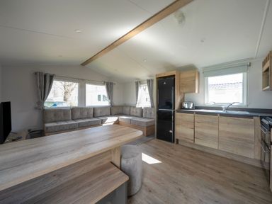 A kitchen and living area with wooden cabinets a black refrigerator a gray couch and a wooden dining table at Kingfisher Caravan - Billing Aquadrome in Billing Aquadrome Holiday Park