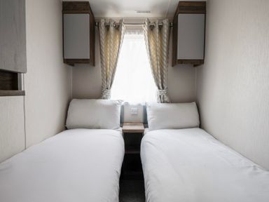 A bedroom with two single beds separated by a small wooden nightstand and a window with curtains at Waterslide Way Billing Aquadrome