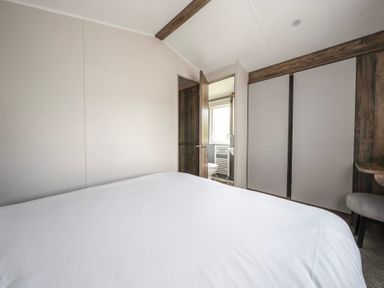 A bedroom with a bed white bedding a door open to a bathroom and a wardrobe at Waterslide Way Billing Aquadrome