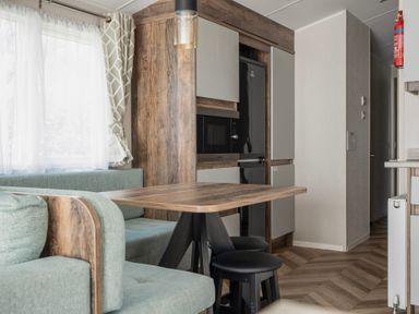 A kitchen and dining area with a wooden table black stools a built-in microwave and refrigerator at Stillwater Retreat - Billing Aquadrome Holiday Park