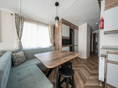 A dining area with an L-shaped sofa around a wooden table and two black stools in a compact space