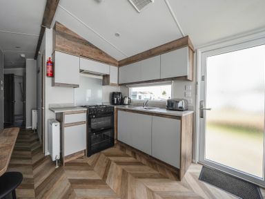 A kitchen with grey cabinets a black oven an air fryer kettle toaster and a frosted glass door at Stillwater Retreat - Billing Aquadrome in Billing Aquadrome Holiday Park