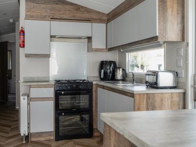 A kitchen with a black oven, silver kettle, black air fryer, silver toaster, and wooden cabinets at Stillwater Retreat Billing Aquadrome