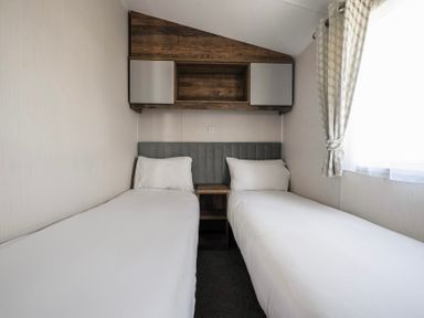 A bedroom with two single beds with a headboard and a shelf above at Stillwater Retreat - Billing Aquadrome in Billing Aquadrome Holiday Park