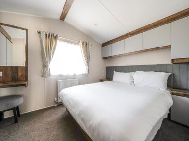 A bedroom with a bed a window with curtains a mirror and a small stool at Stillwater Retreat - Billing Aquadrome Holiday Park