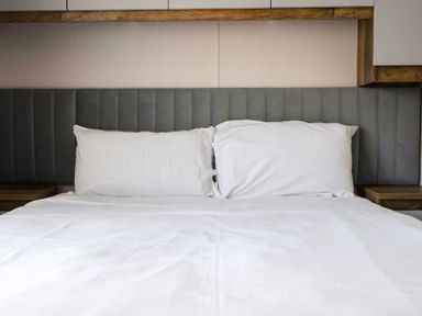 A bed with white sheets and pillows and a grey padded headboard at Stillwater Retreat - Billing Aquadrome Holiday Park